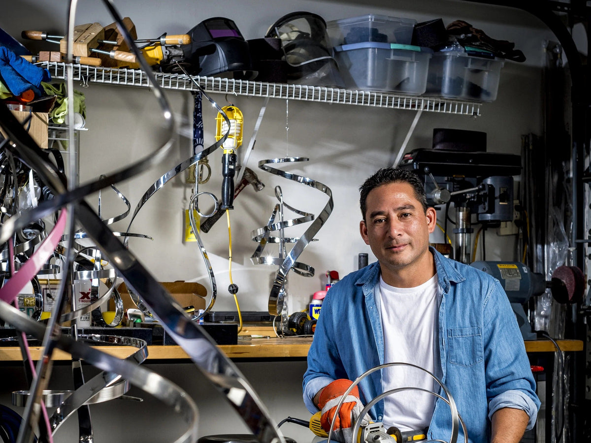 Artist Gary Traczyk seated in his studio, surrounded by his stainless steel sculptures