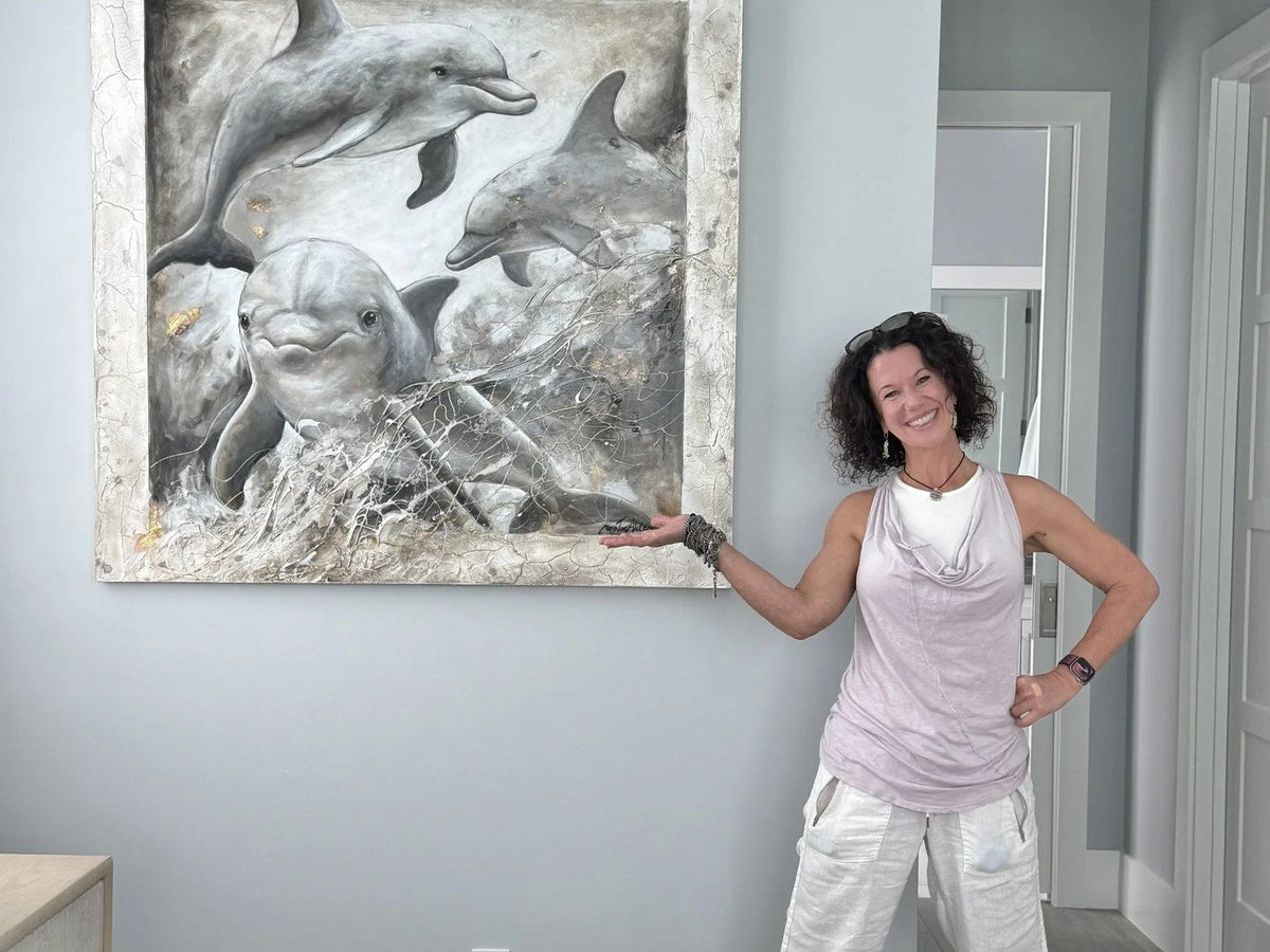 Artist Christine Adele Moore standing beside her painting of three dolphins