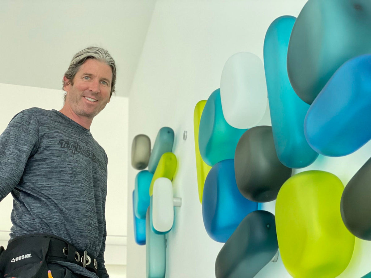 Artist Christopher Jeffries smiling beside one of his Rock Series hand-blown glass walls