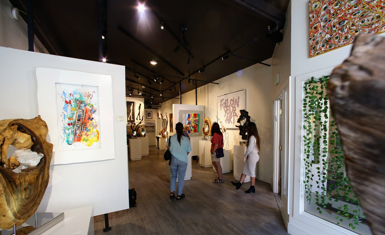 Inside of gallery with customers, sculptures, and paintings
